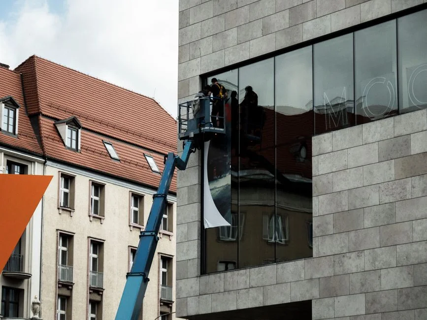 gallery-03 A man is cleaning skyscraper windows with a harness, highlighting work on tall urban buildings.
